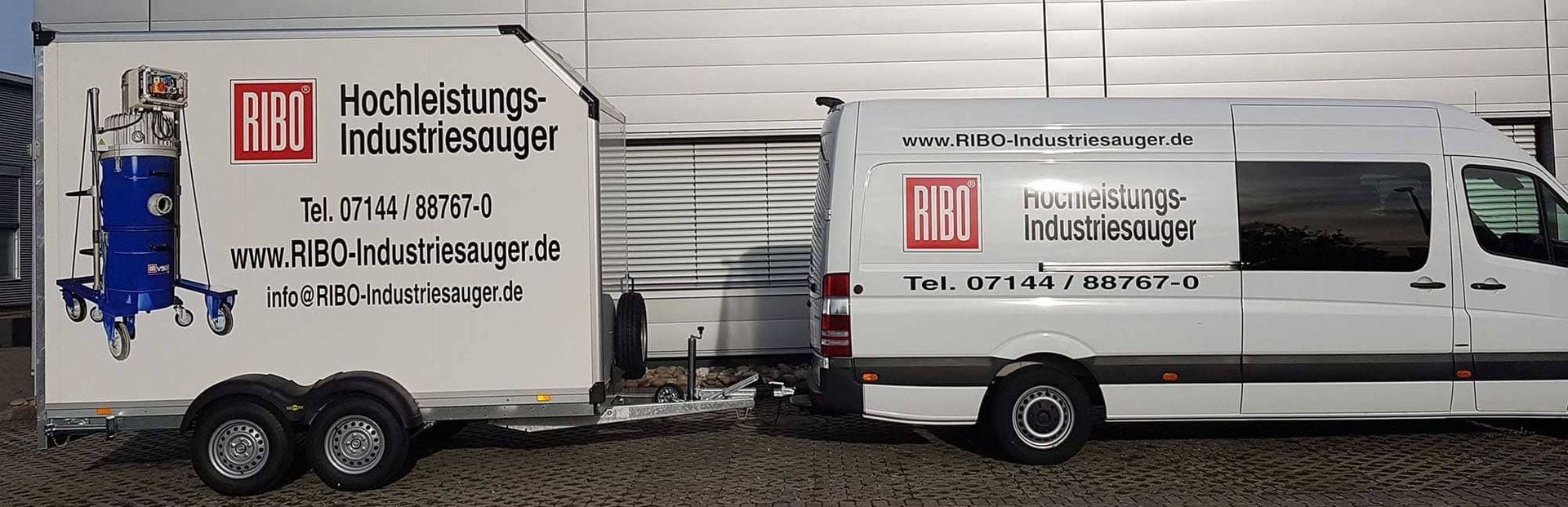 Weißer Transporter und Anhänger mit Aufschrift und Logo von RIBO Hochleistungs-Industriestaubsauger vor einer grauen Halle